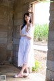 A woman in a white dress leaning against a wall.