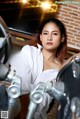 A woman in a white shirt sitting on a motorcycle.