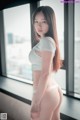 A woman in a white shirt and panties standing by a window.