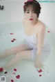 A woman sitting in a bathtub with rose petals on the floor.