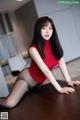 A woman in a red top and black tights sitting on a table.