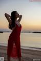 A woman in a red dress standing on a beach.