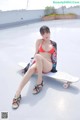 A woman in a bikini sitting on a skateboard.