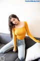 A woman sitting on a couch wearing a yellow top and jeans.