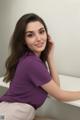 A woman in a purple shirt sitting on a white table.