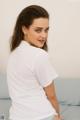 A woman sitting on a bed wearing a white shirt.